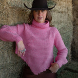 Woman wearing a pink sweater and black cowboy hat standing in front of hay bales.